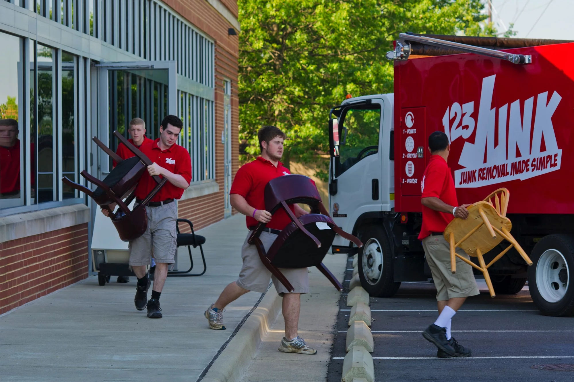 Three junk removal workers carrying chairs out of a building toward a red 123JUNK truck