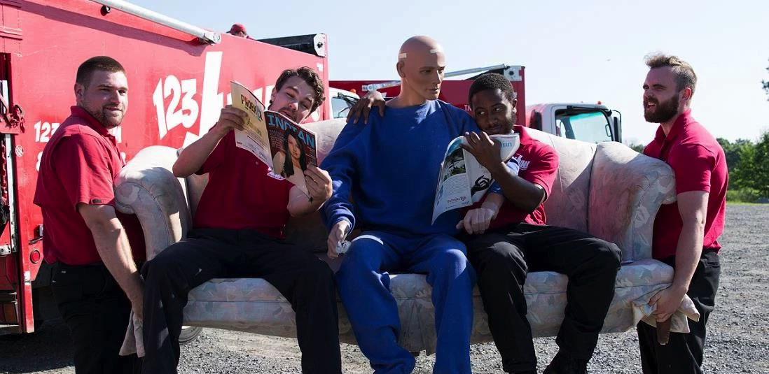 two men moving a couch with three men seated on it