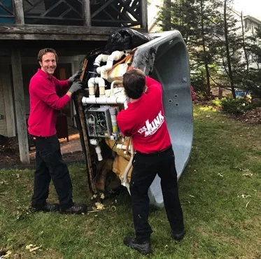 Two workers in red shirts carrying an overturned hot tub outside