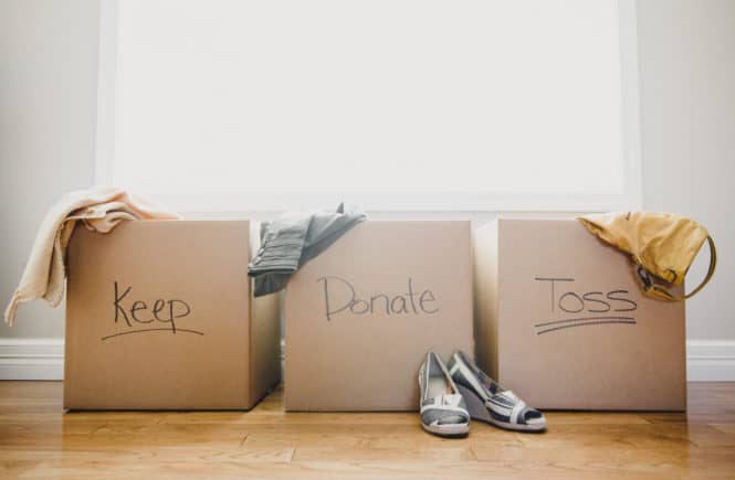 Three cardboard boxes labeled Keep, Donate, and Toss, with clothing and shoes placed around them