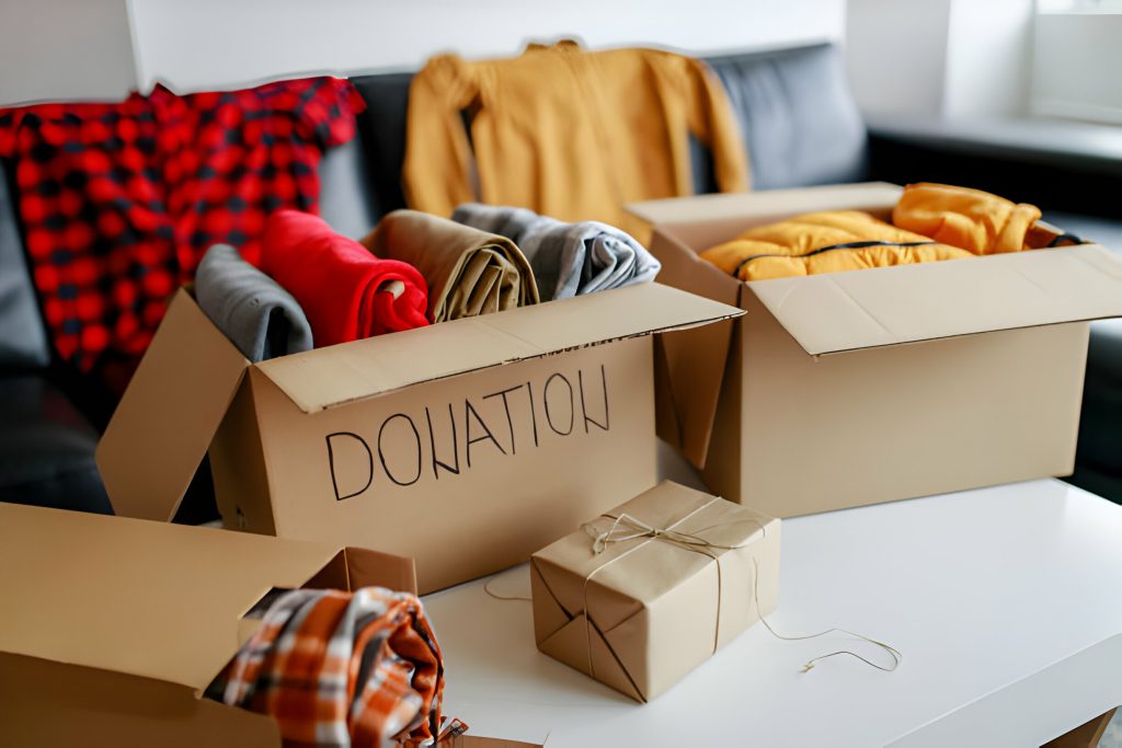 A cardboard boxes labeled “Donation” filled with neatly folded clothes on a table, with more clothing in the background
