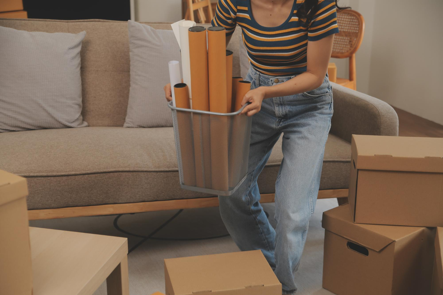 A woman holding a small trash bin filled with rolled-up posters or papers while packing in a living room