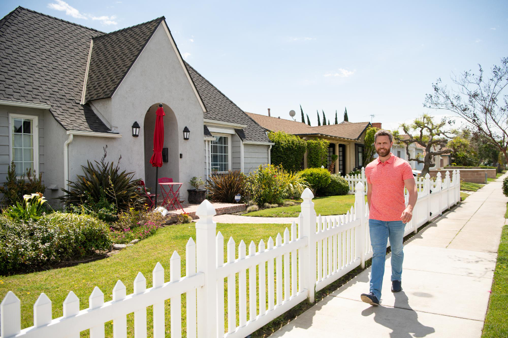 Man walking along the sidewalk in a residential neighborhood with well-maintained lawns, gardens, and attractive curb appeal