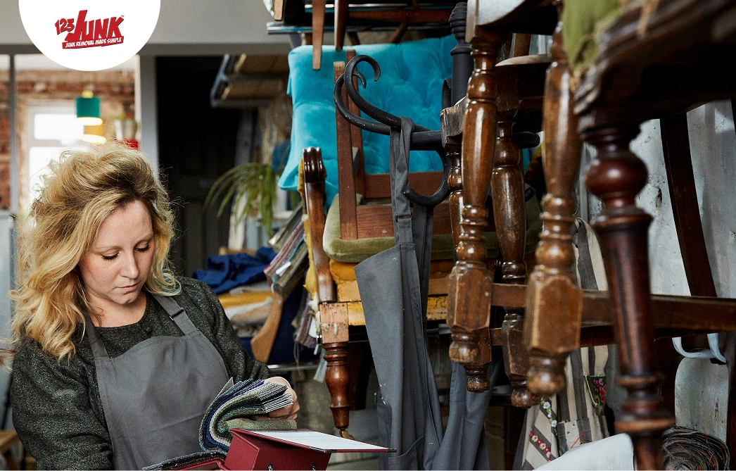 Woman cleaning and refurbishing secondhand furniture in a workshop with stacked chairs